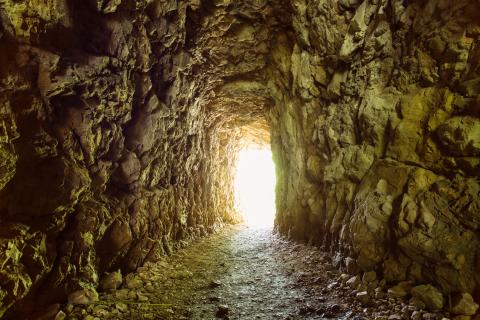 Das Foto zeit einen felsigen Tunnel mit einem hell erleuchteten Ausgang am Ende.