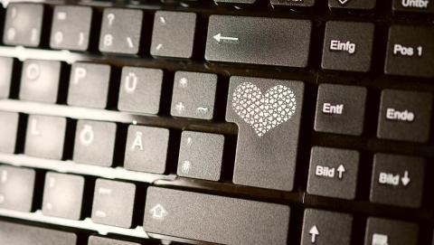 Du siehst einen Teil einer Computertastatur. Der Bereich um die Enter-Taste ist scharf. Auf der Enter-Taste ist ein Herz aus vielen kleinen Herzen aufgedruckt.