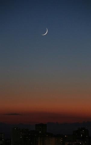 Das Foto zeigt eine feine Mondsichel in der kommenden Nacht über einer Stadt.