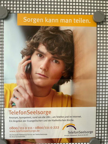 Das Plakat zeigt einen betrübten jungen Mann, der gegen eine Wand lehnt und telefoniert. Darüber steht geschrieben: „Sorgen kann man teilen.“ Darunter steht: „Telefonseelsorge. Anonym, kompetent, rund um die Uhr – am Telefon und in Internet. Ein Angebot der Evangelischen und der Katholischen Kirche. 0800/111 0 111 oder 0800/111 0 222; www.telefonseelsorge.de“