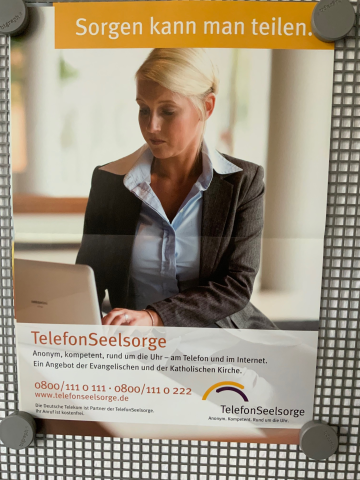 Das Plakat zeigt eine Frau, die an einem Laptop sitzt und etwas schreibt. Darüber steht geschrieben: „Sorgen kann man teilen.“ Darunter steht: „Telefonseelsorge. Anonym, kompetent, rund um die Uhr – am Telefon und in Internet. Ein Angebot der Evangelischen und der Katholischen Kirche. 0800/111 0 111 oder 0800/111 0 222; www.telefonseelsorge.de“