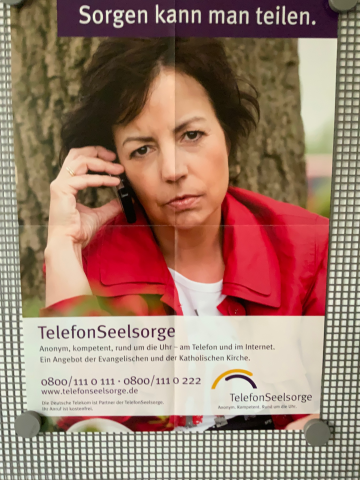 Das Plakat zeigt eine besorgt aussehende Frau, die telefoniert. Darüber steht geschrieben: „Sorgen kann man teilen“. Darunter steht geschrieben: „Telefonseelsorge. Anonym, kompetent, rund um die Uhr – am Telefon und im Internet. Ein Angebot der Evangelischen und der Katholischen Kirche. Telefonnummer 0800/1110111 oder 0800/1110222, www.telefonseelsorge.de“