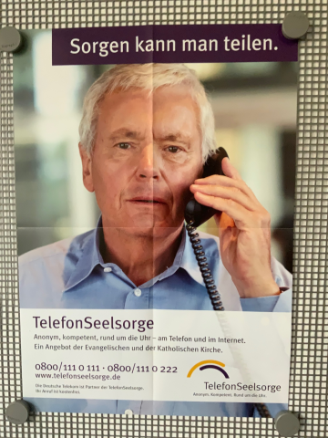 Das Plakat zeigt einen betrübten Mann, der telefoniert. Darüber steht geschrieben: „Sorgen kann man teilen.“ Darunter steht: „Telefonseelsorge. Anonym, kompetent, rund um die Uhr – am Telefon und in Internet. Ein Angebot der Evangelischen und der Katholischen Kirche. 0800/111 0 111 oder 0800/111 0 222; www.telefonseelsorge.de“